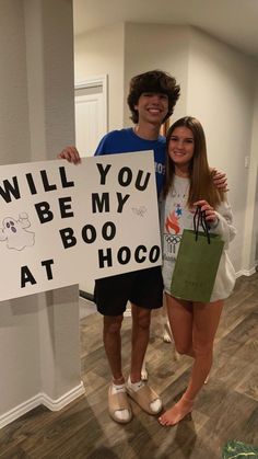 two people are holding up a sign that says will you be my boo at hoco?