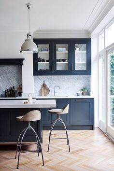 two stools in the middle of a kitchen with blue cabinets and marble counter tops