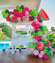 a bunch of balloons and watermelon are on the ground near a pool with a chair