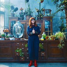 a woman standing in front of a wooden cabinet with plants on it and giving the thumbs up sign