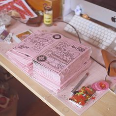 a bunch of pink papers sitting on top of a wooden desk next to a keyboard