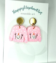 two pink sweaters with reindeer faces on them are hanging from gold - plated hooks