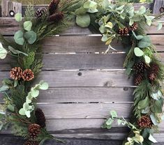 a wreath with pine cones and greenery hanging on a wooden fence