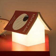 a small house shaped lamp sitting on top of a table next to an alarm clock