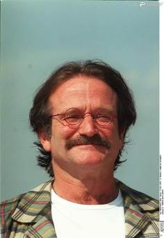 a man with glasses and a moustache looks into the distance while standing in front of a blue sky