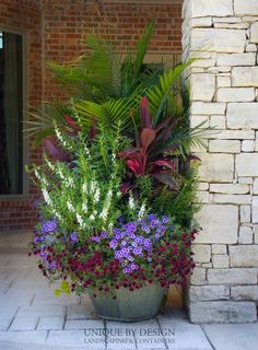 a planter filled with lots of colorful flowers next to a brick wall and door