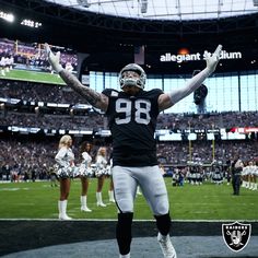 a football player standing on the field with his arms in the air and two cheerleaders behind him