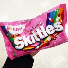 someone holding up a pink skittles candy bar