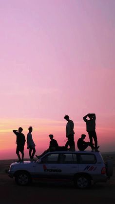 a group of people standing on top of a car in front of the sun setting