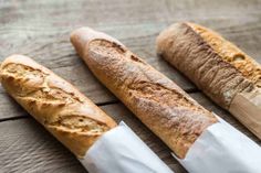 three pieces of bread sitting on top of a wooden table next to a knife and paper bag