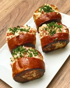 four pieces of bread with various toppings sitting on a white platter atop a wooden table