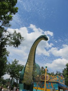 an inflatable dinosaur ride with people standing around it on a sunny day at the amusement park