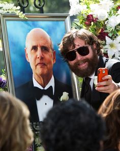 a man taking a selfie in front of a portrait of an old man with sunglasses