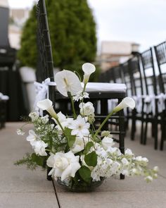 a vase filled with white flowers sitting on top of a sidewalk next to black chairs