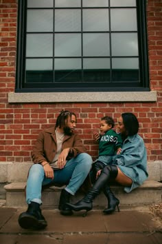 a man, woman and child sitting on a bench in front of a brick building