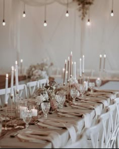 a long table with white chairs and candles