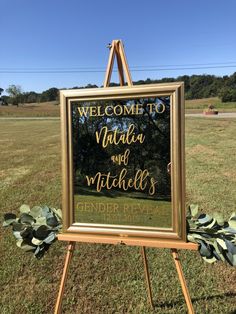 a welcome sign in the middle of a field with flowers around it and an easel