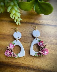 the earrings are decorated with pink flowers and green leaves on top of a wooden table