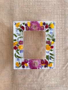 a white frame with flowers painted on it sitting on top of a cloth covered surface