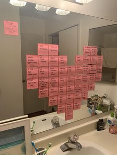 a bathroom mirror with pink sticky notes attached to it's sides and on top of the mirror is a sink