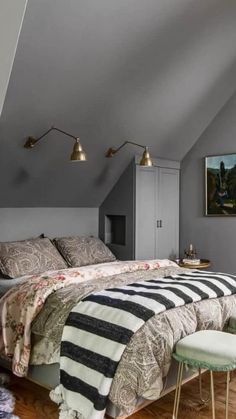 an attic bedroom with gray walls and wooden flooring, two stools on either side of the bed