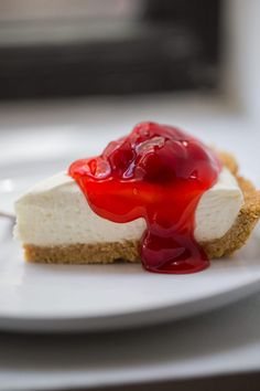 a piece of cheesecake on a white plate with red sauce drizzled over it