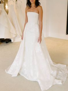 a woman in a white wedding dress standing next to some dresses on display at a bridal event