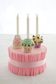 three cupcakes and four candles on a pink cake with ruffle skirting