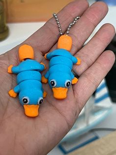 two blue and orange plastic fish keychains are held in someone's hand