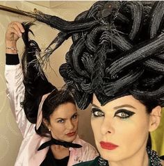 two women with black hair and makeup are posing for the camera while one woman is holding up her hair