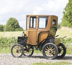 an old - fashioned car is parked on the side of the road in front of a grassy field