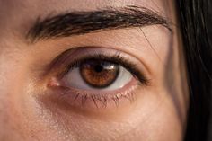 the eye of a woman with long black hair and brown eyes is shown in this close up photo