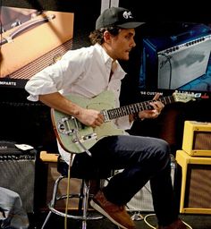 a man sitting on top of a stool playing an electric guitar in front of a tv