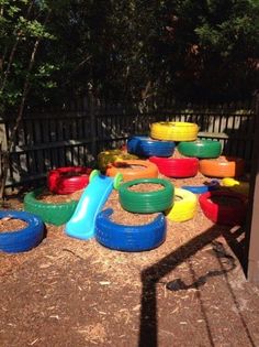 an outdoor play area with many different colored plastic tires and rings on the ground in front of a fence