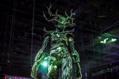 a statue of an alien standing in front of a stage with green lights on it