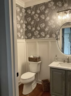 a white toilet sitting under a bathroom mirror next to a wooden sink vanity with baskets on it