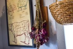 some flowers are hanging on the wall next to two pictures and a basket with dried flowers in it