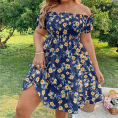 a woman in a blue floral print dress standing on a picnic table with her legs crossed