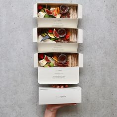 three boxes filled with different types of food on top of each other in front of a person's hand