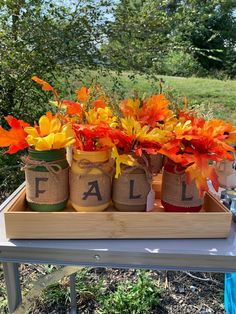 three jars filled with fall flowers sitting on top of a wooden tray in the grass