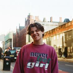 a young man standing on the sidewalk in front of some buildings smiling at the camera