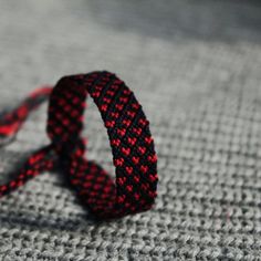 a red and black bracelet laying on top of a gray blanket