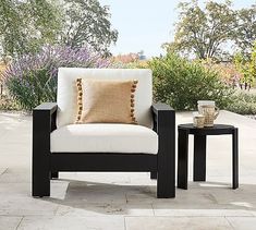 a chair and side table sitting on a patio with flowers in the backgroud