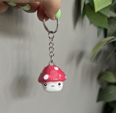 a hand holding a keychain with a mushroom on it's side and a green plant in the background