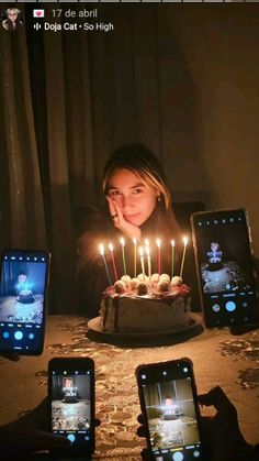 a woman sitting in front of a cake with lit candles on it and three cell phones next to her