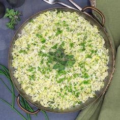 there is rice in the pan with green onions and parsley on the table next to it