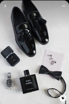 a pair of black shoes, watch and tie on a white surface