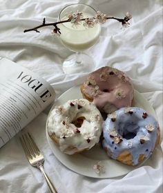 three doughnuts on a plate next to a glass of milk and a book