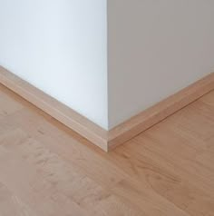 the corner of a room with wood flooring and white paint on it's walls