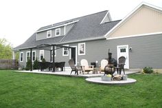 a patio with chairs and tables in front of a large gray house on the grass